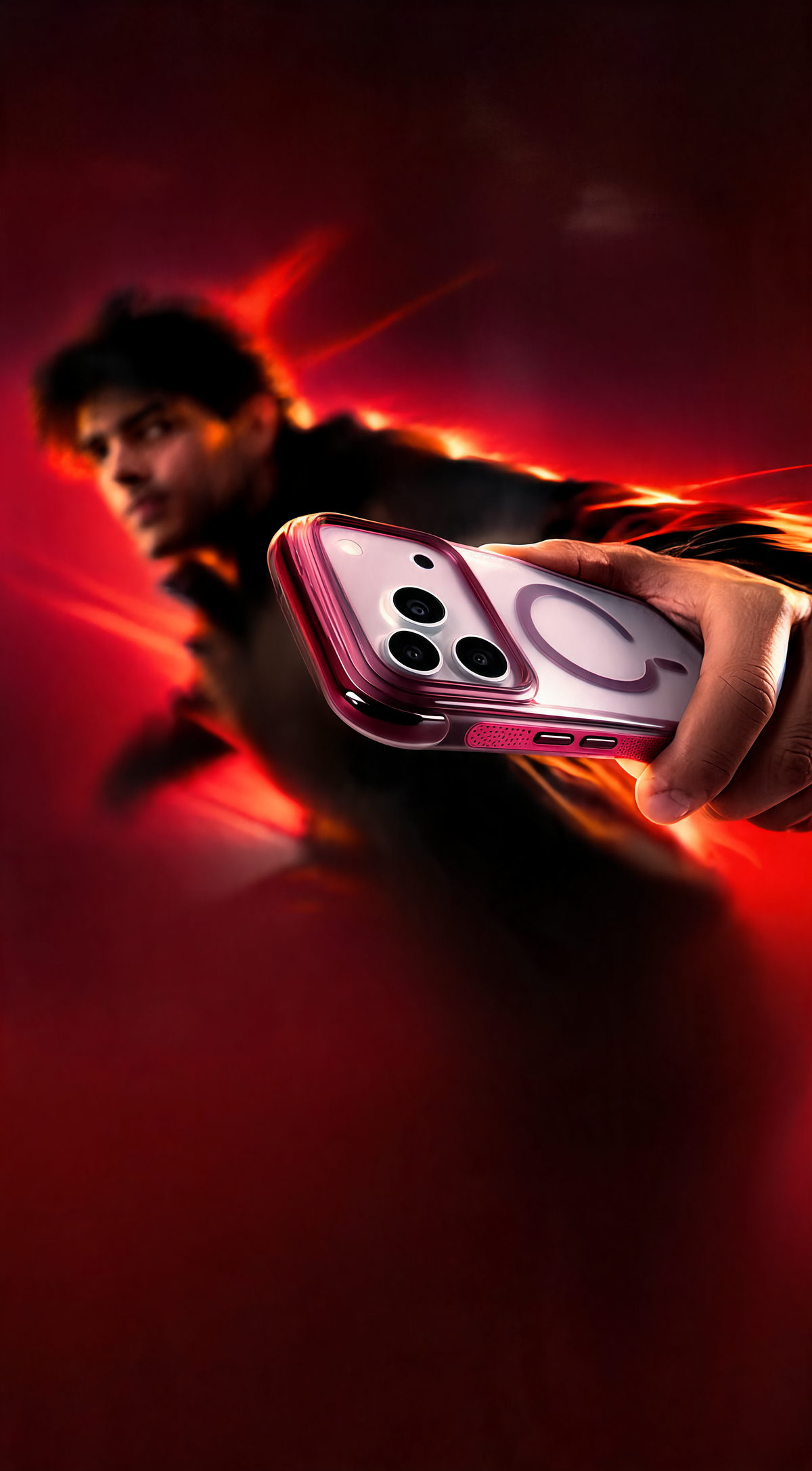 A hand holds a smartphone with a pink and white MagSafe case against a dramatic dark red and black background with glowing orange light streaks and a blurred person in the background.